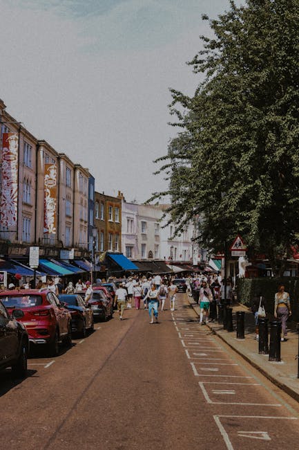 A narrow urban alleyway during daytime with overcast sky, featuring a single white arrow painted on the asphalt pointing forward. On both sides of the alley are multi-storey buildings, with the left s